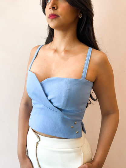 Woman wearing a light blue top with button details against a beige background