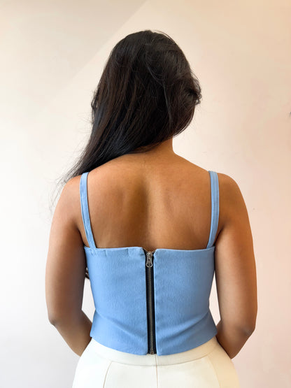 Person wearing a light blue corset-style top with a zipper back against a plain background
